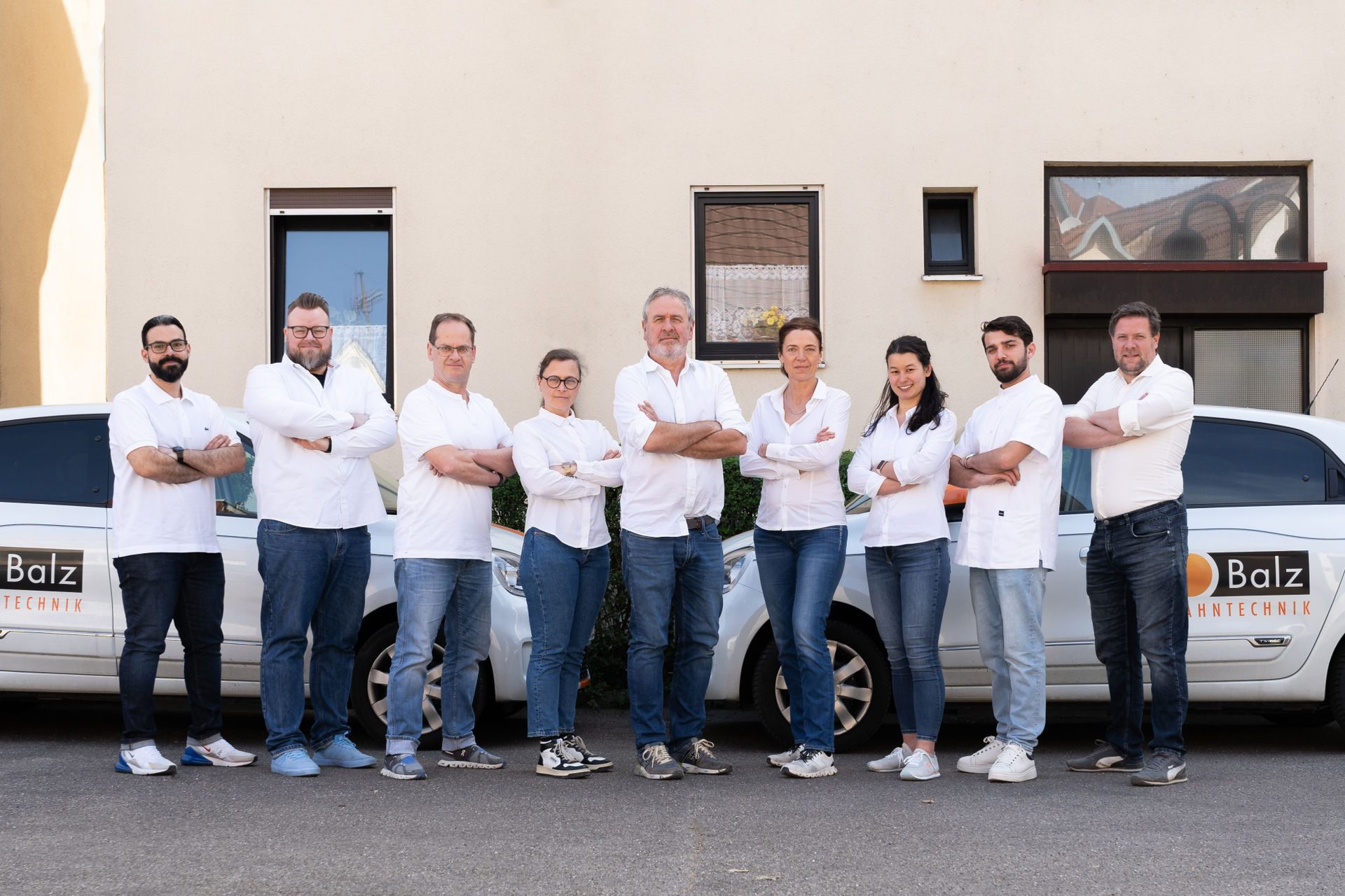 Das Team von Zahntechnik Balz in weißen Hemden vor den Firmenwagen mit Balz-Logo
