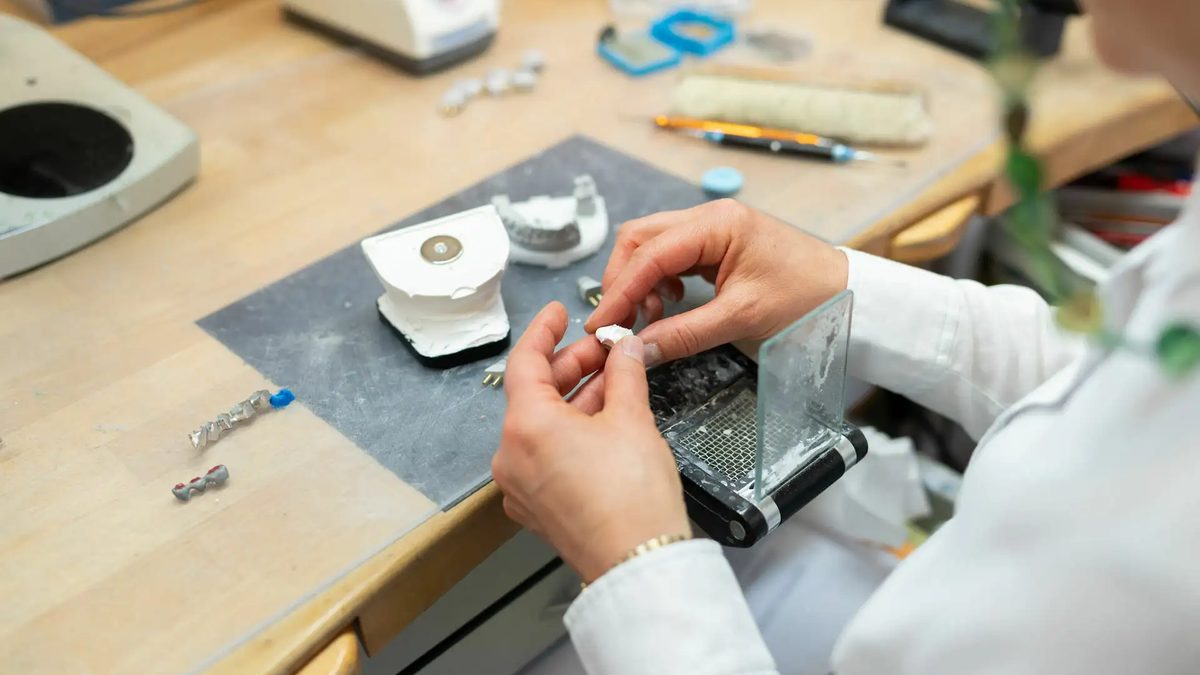 Hände bei der Arbeit an einem Zahnmodell auf dem Labortisch