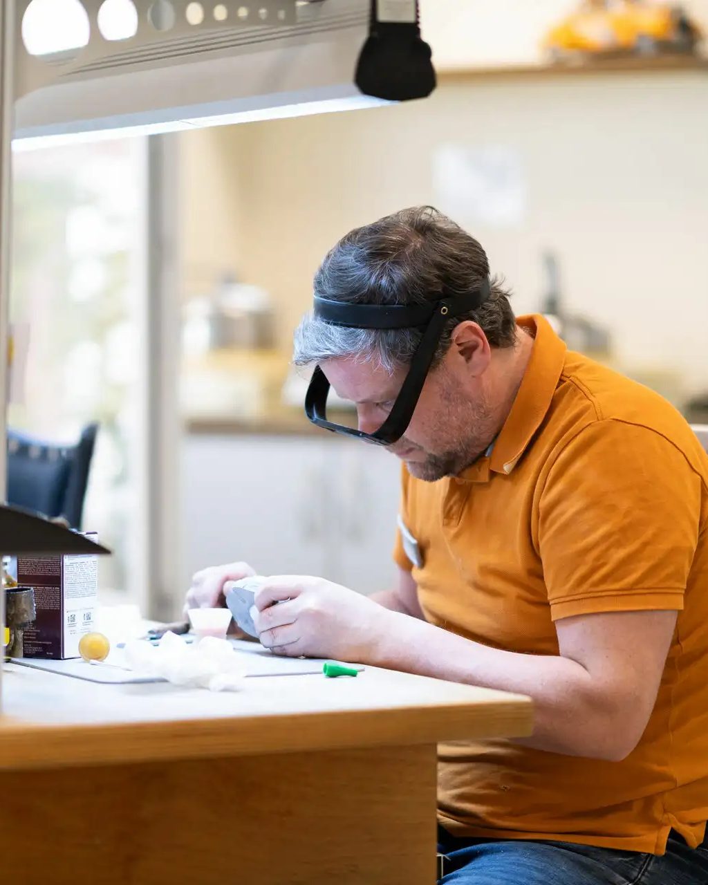 Zahntechniker mit Lupenbrille arbeitet konzentriert am Laborplatz